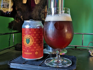 A bottle of Saints Row Harvest next to a tulip glass filled with the bottle's contents, a garnet colored, clear beer with a near white head