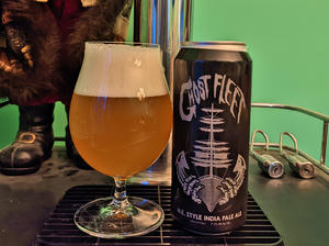 A bottle of Vanish Ghost Fleet next to a tulip glass filled with the bottle's contents, a hazy, dark gold beer with a thick white head