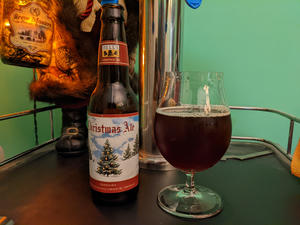 A bottle of Bell's Christmas ale next to a tulip glass filled with its contents, a dark mahogany beer with a tan, thick head