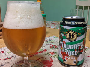 A can of Devils Backbone Nughty or Nice cold IPA next to a tulip shaped glass filled with the can's contents, a golden beer with a thick, fluffy white head