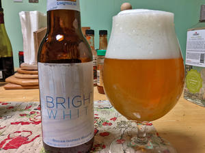 A bottle of Bell's Bright White next to a tulip glass filled with the bottle's contents, a light copper, hazy beer with a fluffy white head