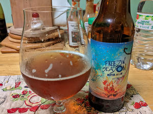 A bottle of Flying Dog Freezin' Season winter ale next to a tulip shaped glass filled with the can's contents, brown beer with a collar of tan foam