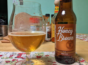 An empty bottle of beer, labeled 'Genesee Specialty Honey Brown`, next to a tulip shaped glass filled with the bottle's contents. The beer is straw gold and very clear