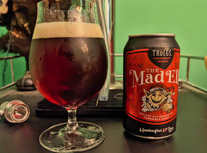 A bottle of Troegs Mad Elf next to a tulip glass filled with the bottle's contents, a dark, clear beer the color of mahogany with a think tan head